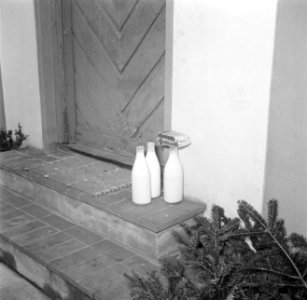 Flessen melk en pakjes boter staan op de stoep bij de voordeur, Bestanddeelnr 252-8730