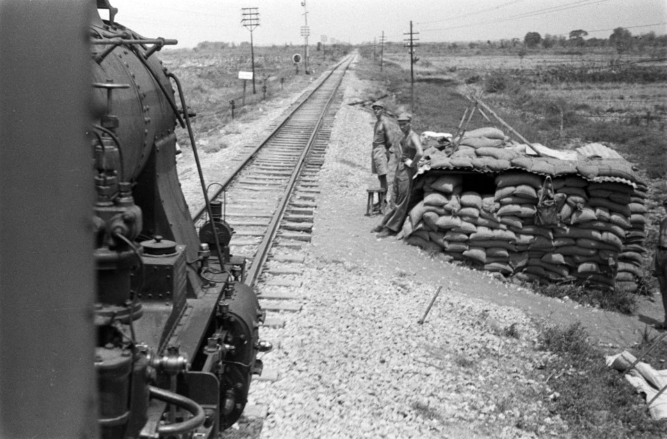 Foto genomen uit trein. Locomotief passeert een met zandzakken versterkte contro, Bestanddeelnr 65-4-4