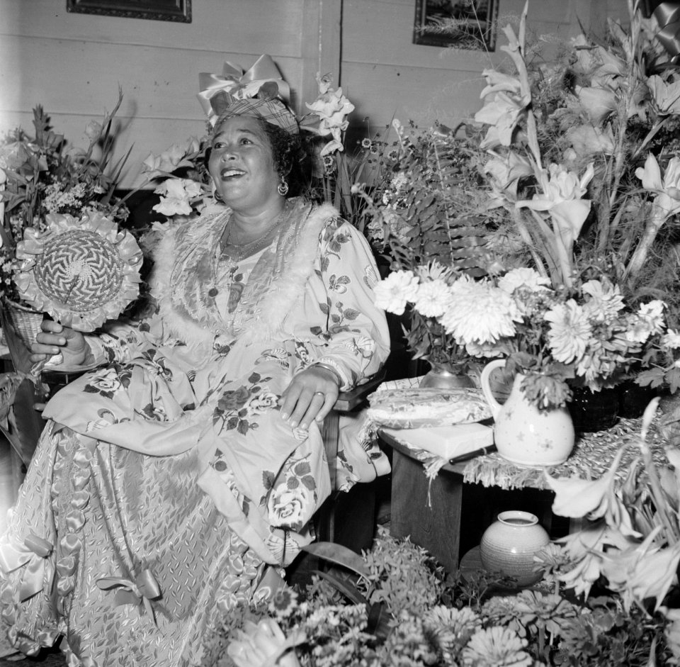 Feestelijk geklede vrouw temidden van bloemen bij een feest in Paramaribo, Bestanddeelnr 252-2454