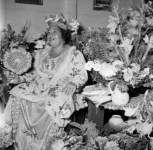 Feestelijk geklede vrouw temidden van bloemen bij een feest in Paramaribo, Bestanddeelnr 252-2454