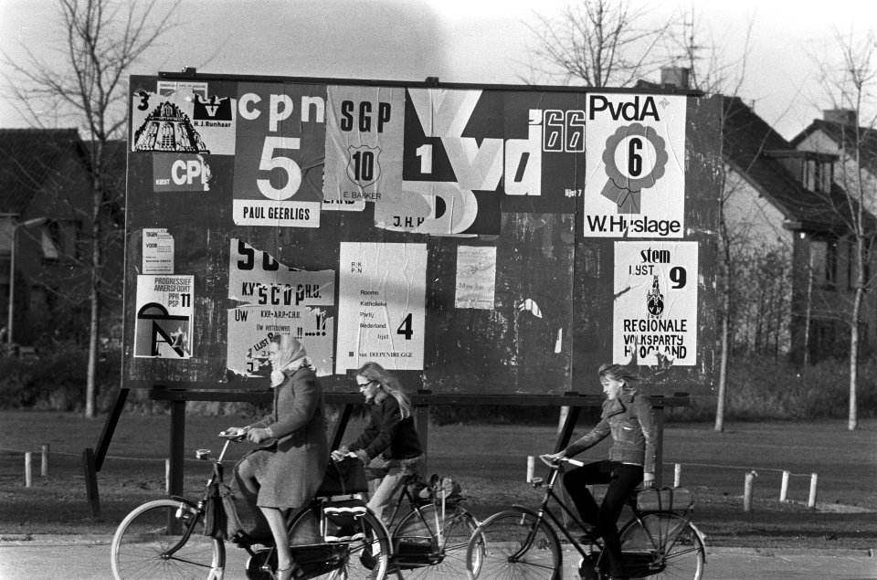 Fietsers passeren een aanplakbord met affiches, Bestanddeelnr 926-8412