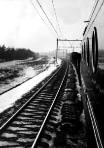 Gezicht vanaf een in een goederentrein meegevoerde electrische locomotief uit de serie 1100 van de NS op de besneeuwde spoorbaan tussen Amersfoort en 