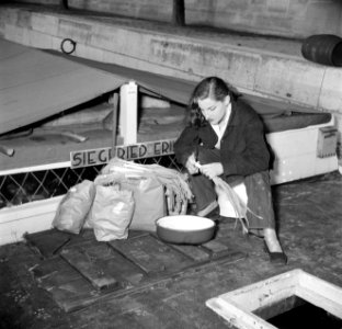 Gezeten aan dek van een schip, snijdt een vrouw de prei naast haar staan tassen, Bestanddeelnr 252-9401