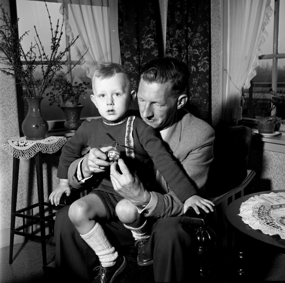 Gerard met zijn zoontje Gerrie op schoot terwijl hij een speelgoedhelikopter in , Bestanddeelnr 254-3310