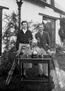 Gentleman and lady with golf clubs and three trophies (1293369)