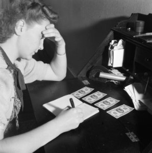 Geldzuivering Een vrouw noteert iets in een schrift Voor haar liggen vier bank, Bestanddeelnr 900-8316