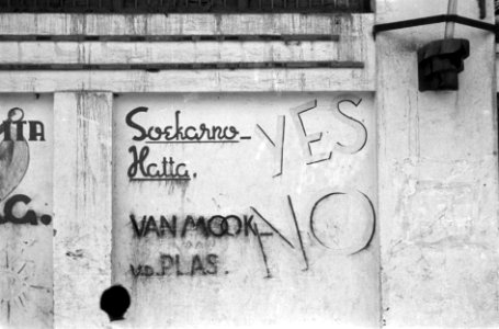 Graffiti op muren ¨Soekarna-Hatta YES Van Mook v.d. Plas NO¨. Voor de muur staa…, Bestanddeelnr 5421