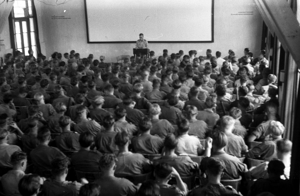 Grote groep militairen in een filmzaal worden toegesproken door een man achter , Bestanddeelnr 2931