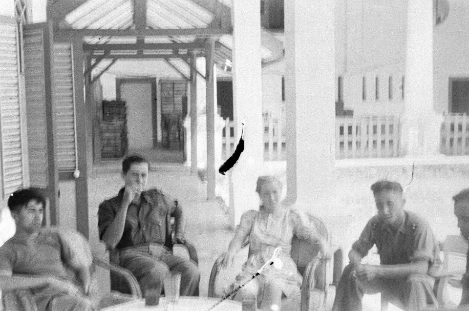 Groep geuniformeerde mannen en een vrouw zitten op een veranda, Bestanddeelnr 52-6-3