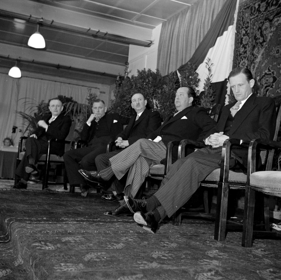 Groep mannen zittend op een podium, waaronder de fabrieksdirecteuren Albert en J, Bestanddeelnr 255-8573