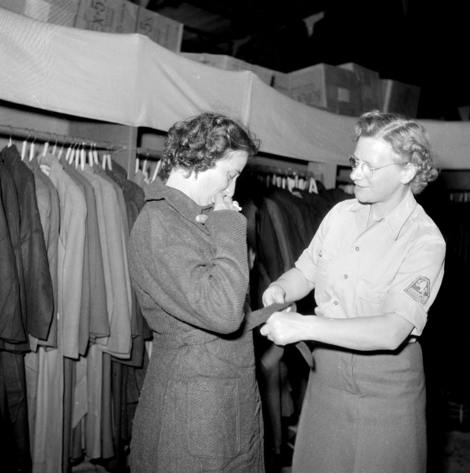 Het kledingcentrum in Ataka een vrouw past een overjas, bijgestaan door een lid, Bestanddeelnr 255-6937