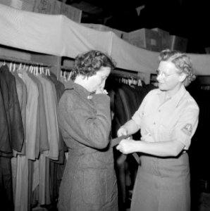 Het kledingcentrum in Ataka een vrouw past een overjas, bijgestaan door een lid, Bestanddeelnr 255-6937