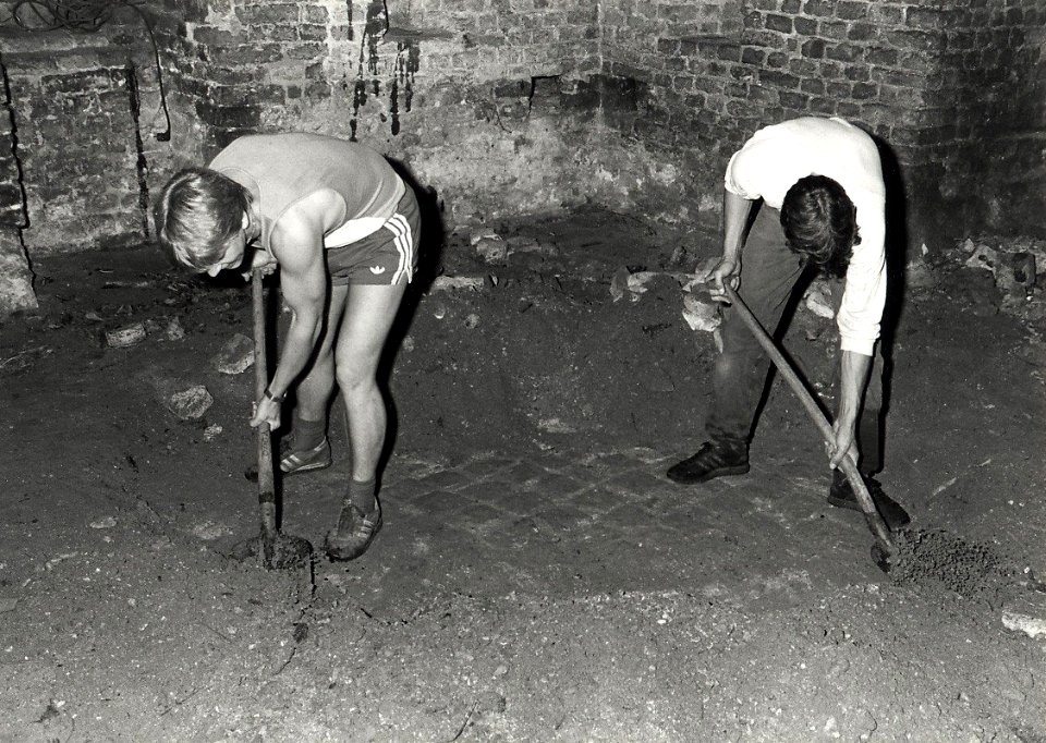 Het 'Afpellen' van de aardlaag waaronder eeuwenlang een duurzame baksteenvloer verborgen heeft gelegen in de kapeltoren. Aangekocht in 1983 van fotograaf C. de Boer. - Negatiefnummer 23189 k, NL-HlmNHA 54013846
