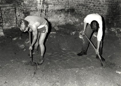 Het 'Afpellen' van de aardlaag waaronder eeuwenlang een duurzame baksteenvloer verborgen heeft gelegen in de kapeltoren. Aangekocht in 1983 van fotograaf C. de Boer. - Negatiefnummer 23189 k, NL-HlmNHA 54013846