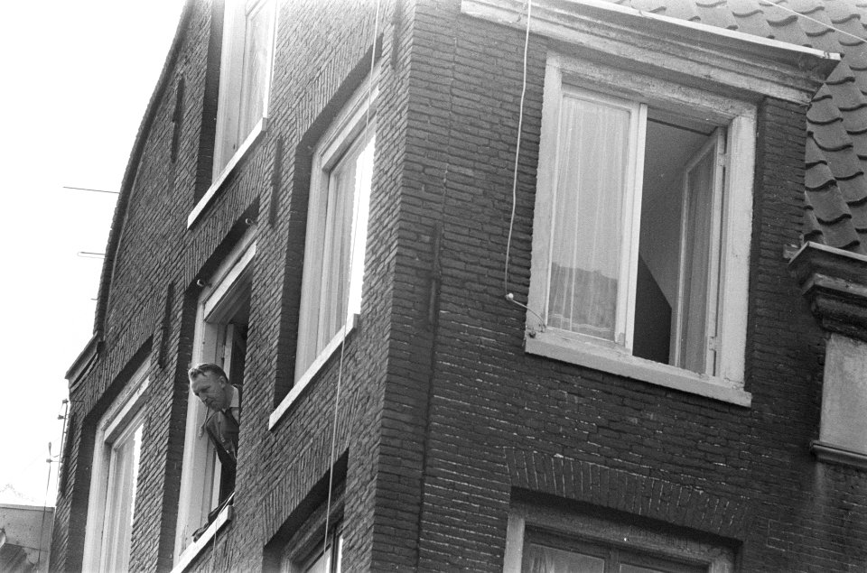 Het huis waar de moordenaar zich verschanste. Uit het raam kijkt een politieman, Bestanddeelnr 921-5853