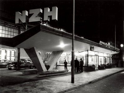 Het nieuwe gebouw van de NZH, ontworpen door Willem Bollebakker, bestemd voor kaartverkoop en wachtruimte aan het Stationsplein, bij avond. Aangekocht in 1977 van United Photos de Boer bv, NL-HlmNHA 54004412