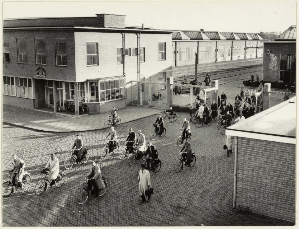 Het personeel fietst huiswaarts door de hoofdingang van de Centrale Werkplaats van de N.S. aan de Amsterdamse Vaart. NL-HlmNHA 54004582