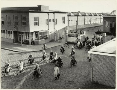 Het personeel fietst huiswaarts door de hoofdingang van de Centrale Werkplaats van de N.S. aan de Amsterdamse Vaart. NL-HlmNHA 54004582
