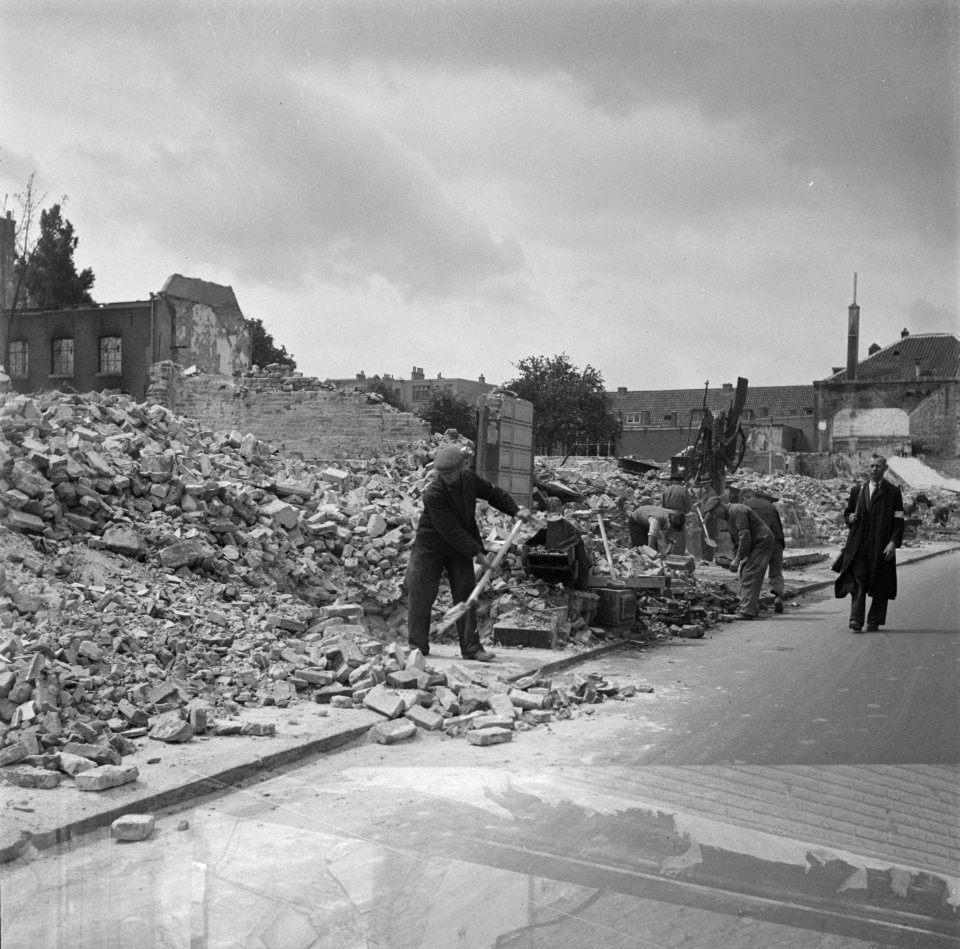 Het puin wordt geruimd. Rechts loopt een gewapende man van Cordon F, Bestanddeelnr 900-4251