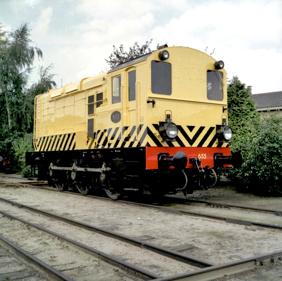 HUA-151542-Afbeelding van de diesel electrische rangeerlocomotief nr 633 serie 600 van de NS in gele uitvoering en met schrikstrepen bij de NS werkplaats te Tilb