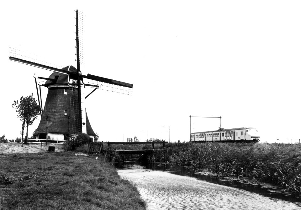 HUA-151336-Gezicht op een molen in een polderlandschap met op de achtergrond een electrisch treinstel plan V mat 1964 van de NS ter hoogte van Hazerswoude