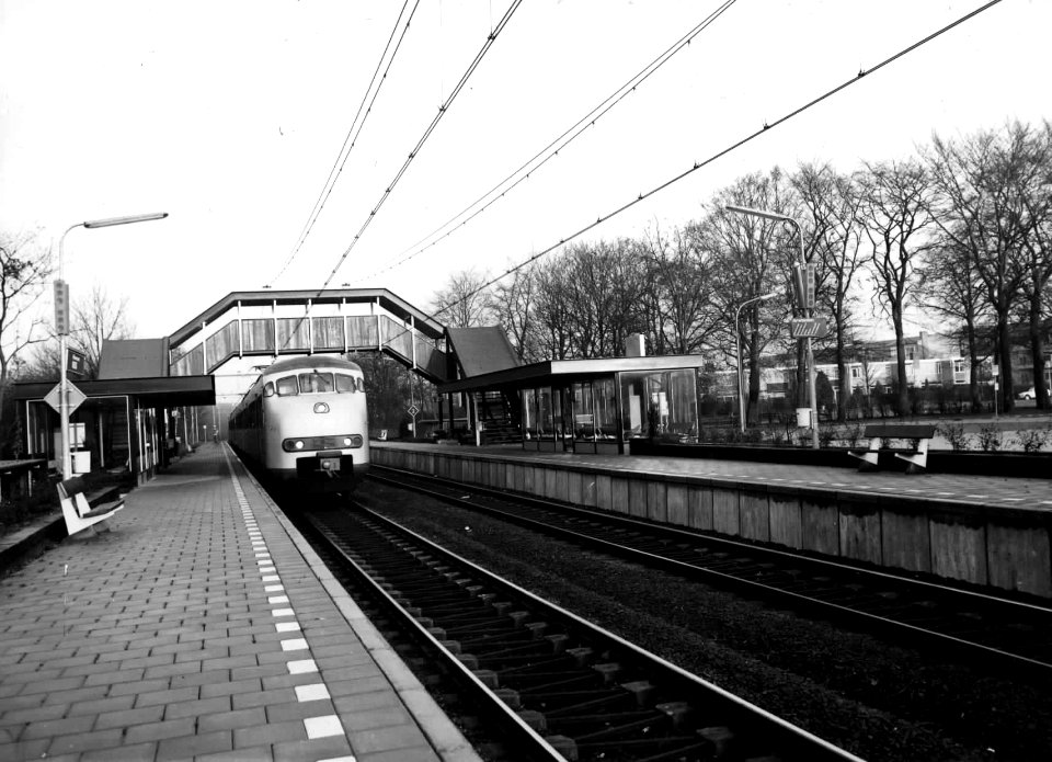 HUA-150439-Gezicht op perrons, voetgangersbrug en sporen van het N.S.-station Hilversum N.O.S. te Hilversum met langs het perron een electrisch treinstel plan T (mat. 1964) van de N.S. De naam Hilversum N.O.S. i