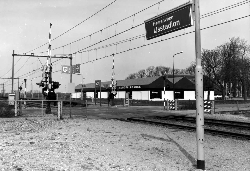 HUA-150398-Gezicht op de overweg en het N.S.-station Heerenveen-IJsstadion met de hallen van Europa Meubel te Heerenveen