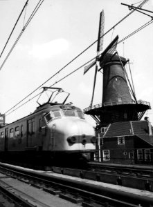 HUA-151895-Afbeelding van een electrisch treinstel mat. 1954 van de N.S. op het spoorviaduct te Delft, met rechts de molen De Roos aan de Phoenixstraat