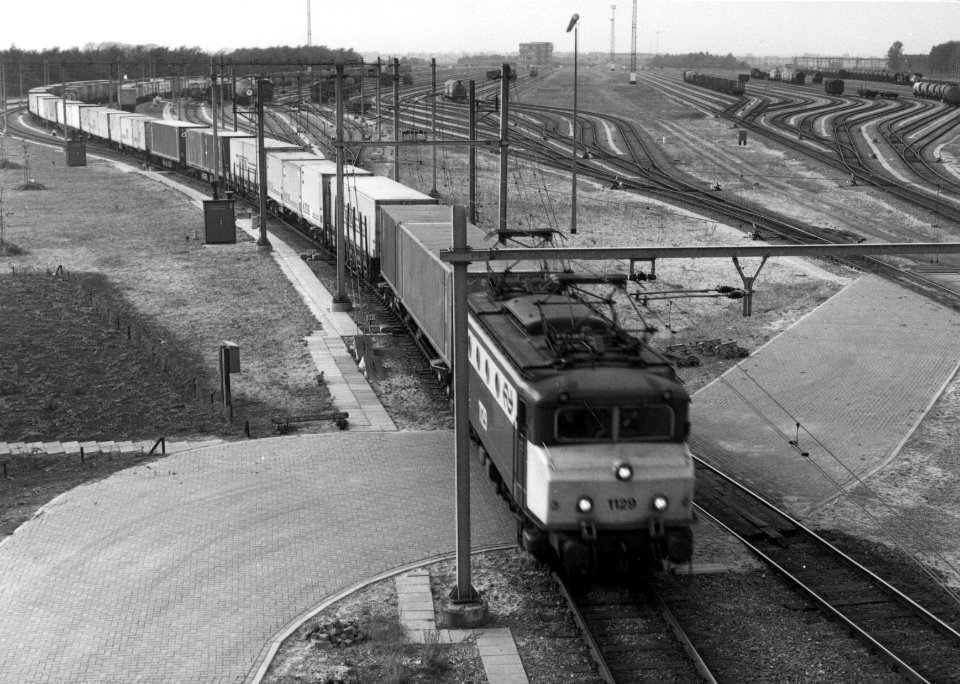 HUA-154904-Afbeelding van de electrische locomotief nr. 1129 (serie 1100) van de N.S. met een containertrein op het rangeerterrein Kijfhoek