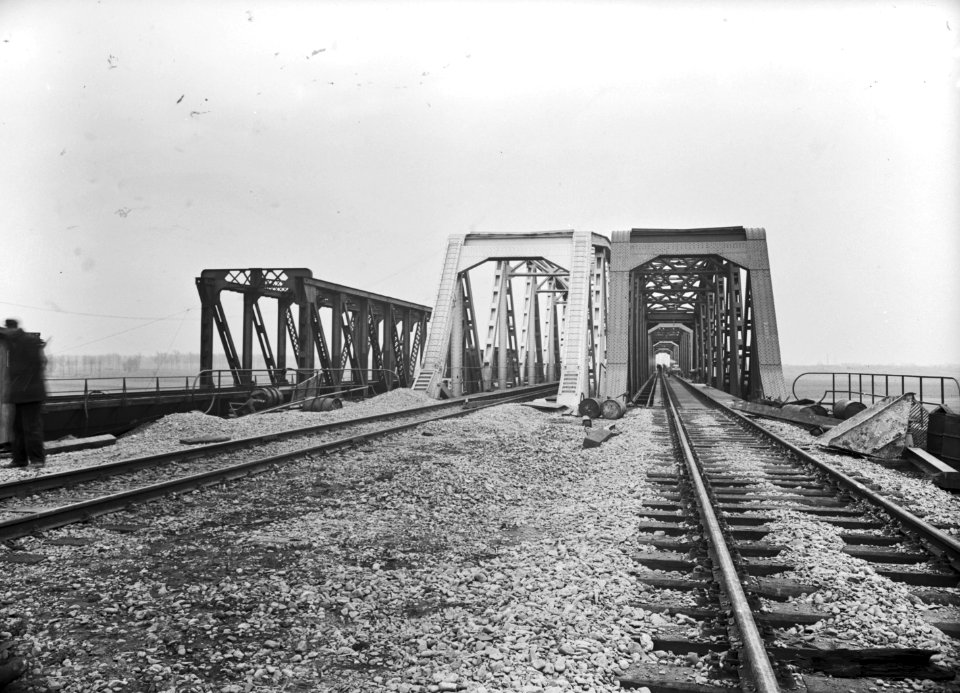 HUA-154938-Gezicht op de spoorbruggen over de Maas te Buggenum. Links de noodbrug uit 1946 en rechts de in aanbouw zijnde definitieve brug