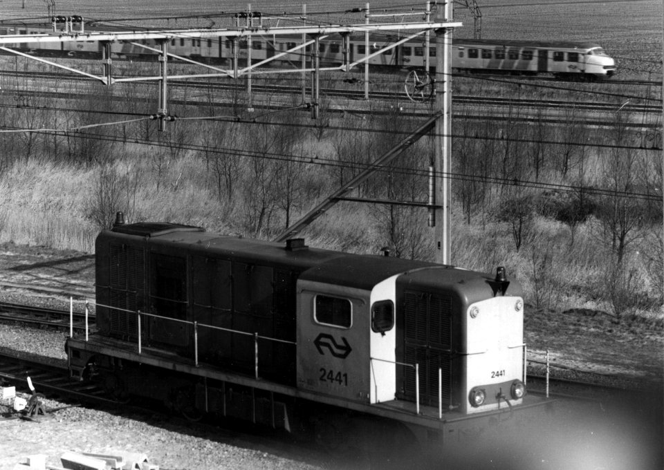 HUA-154895-Afbeelding van de rangerende diesel-electrische locomotief nr. 2441 (serie 2400-2500) van de N.S. op het rangeerterrein Kijfhoek met op de achtergrond een electrisch treinstel mat. 1964 (plan T) van d