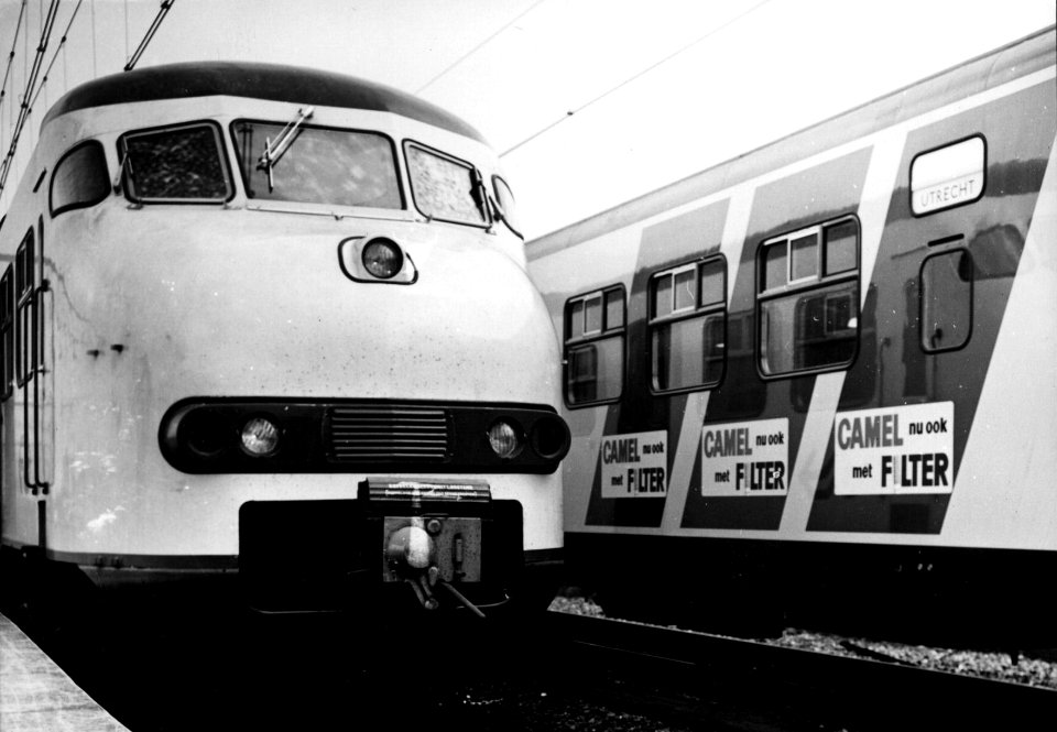 HUA-155616-Afbeelding van de blauwe reclamebanen op de zijwand van een electrisch treinstel mat. 1964 (plan V) van de N.S. met links de kop van een ander treinstel van dit type, beide in de nieuwe, gele huisstij