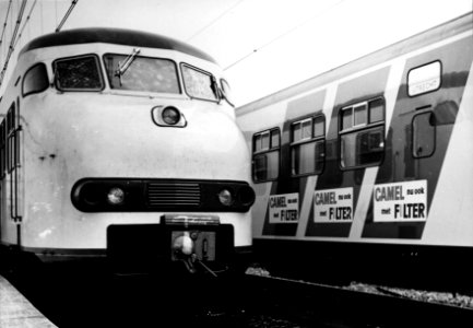 HUA-155616-Afbeelding van de blauwe reclamebanen op de zijwand van een electrisch treinstel mat. 1964 (plan V) van de N.S. met links de kop van een ander treinstel van dit type, beide in de nieuwe, gele huisstij
