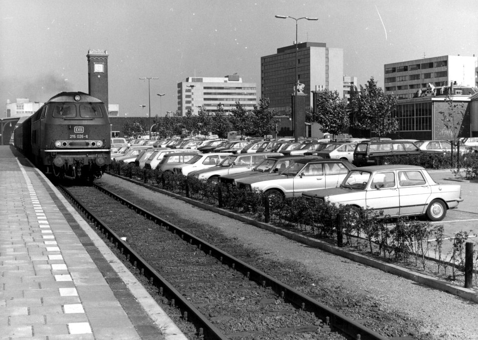 HUA-154561-Gezicht op de P+R-parkeerplaats van het N.S.-station Nijmegen te Nijmegen met links diesellocomotief 215 026-6 van de D.B. met de trein naar Kleve