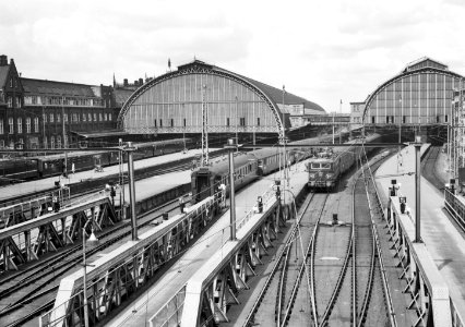 HUA-155853-Gezicht op de sporen aan de oostzijde van het N.S.-station Amsterdam C.S. te Amsterdam met rechts de electrische locomotief nr. 1142 (serie 1100) van de N.S. met rijtuigen en op de achtergrond de perr