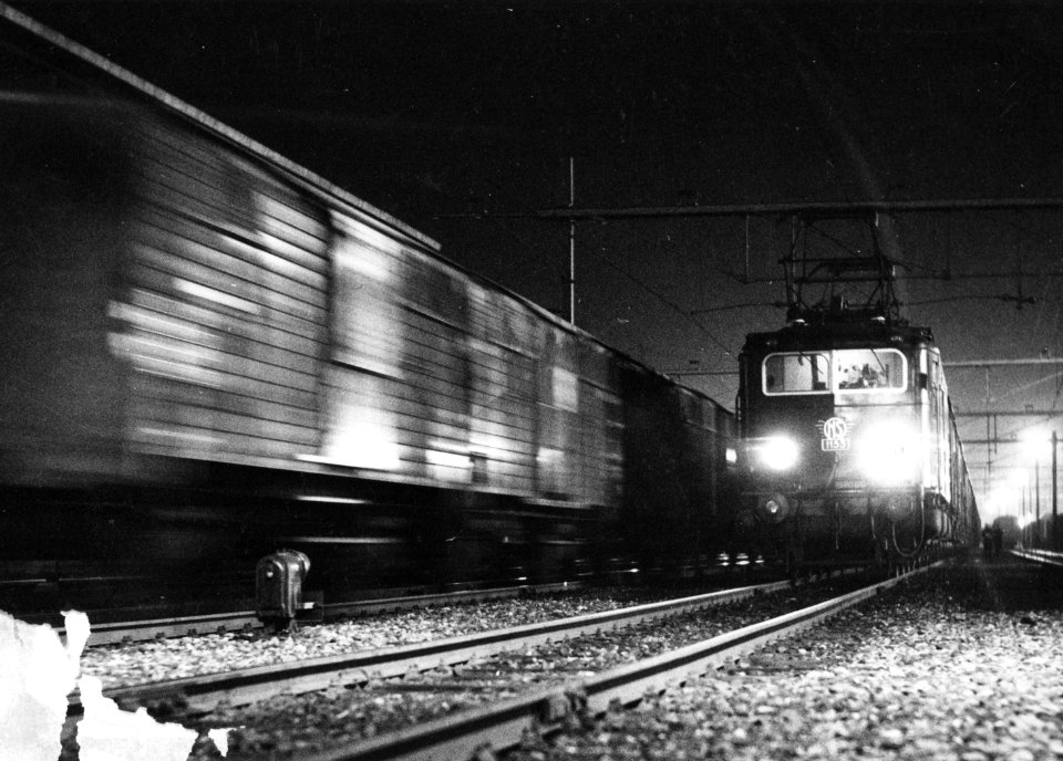 HUA-151117-Afbeelding van de electrische locomotief nr 1153 serie 1100 met goederenwagens bij avond