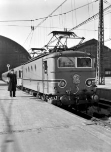 HUA-151107-Afbeelding van de electrische locomotief nr. 1102 (serie 1100) met rijtuigen plan D van de N.S. in turkooise beschildering langs het perron van het N.S.-station Amsterdam C.S. te Amsterdam. De perronc