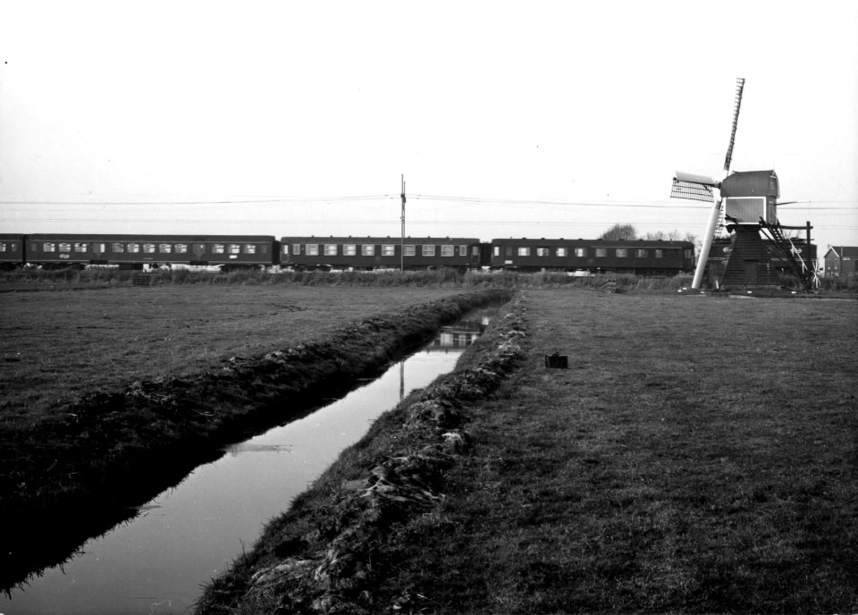 HUA-151050-Gezicht op een weidelandschap met sloot en de Lageveensemolen in Lisse, met op de achtergrond een getrokken trein met internationale rijtuigen