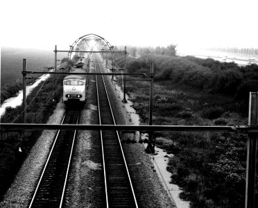 HUA-151074-Gezicht op een electrisch treinstel mat. 1964 (plan T) van de N.S. ter hoogte van Maartensdijk, met op de achtergrond ronde, betonnen bovenleidingsportalen
