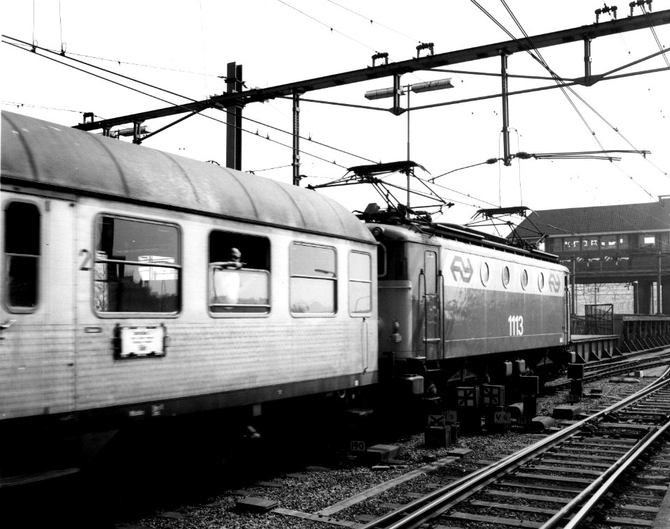 HUA-151136-Afbeelding van de (gehuisstijlde) electrische locomotief nr. 1113 (serie 1100) van de N.S. met een buurlandtrein naar Köln bij vertrek uit het N.S.-station Amsterdam C.S. te Amsterdam. Geheel rechts h