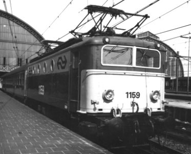 HUA-151128-Afbeelding van de electrische locomotief nr. 1159 (serie 1100) van de N.S. met internationale rijtuigen langs het perron van het N.S.-station Amsterdam C.S. te Amsterdam