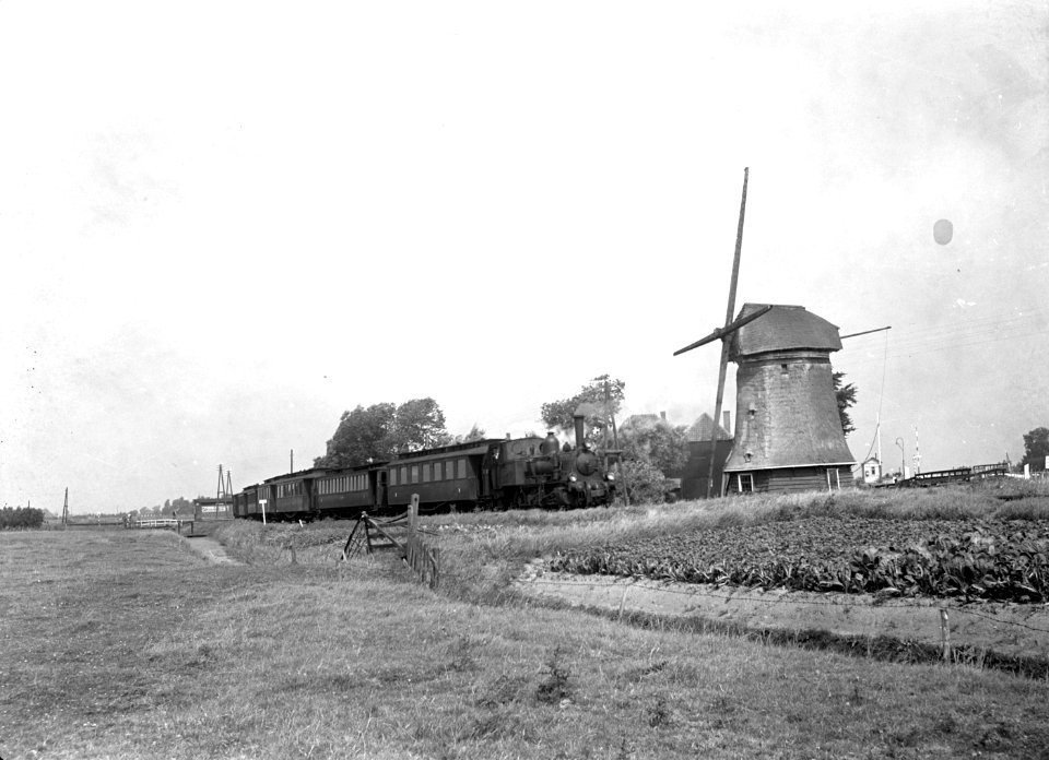 HUA-151329-Afbeelding van de stoomlocomotief nr. 7742 (serie 7700, "Bello") van de N.S. met rijtuigen in een landschap met molen te Koedijk
