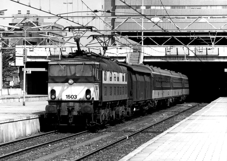 HUA-151973-Afbeelding van de electrische locomotief nr. 1503 (serie 1500) van de N.S. met een bagagerijtuig ("stalen D") en rijruigen ICR langs een perron van het N.S.-station Den Haag CS te Den Haag