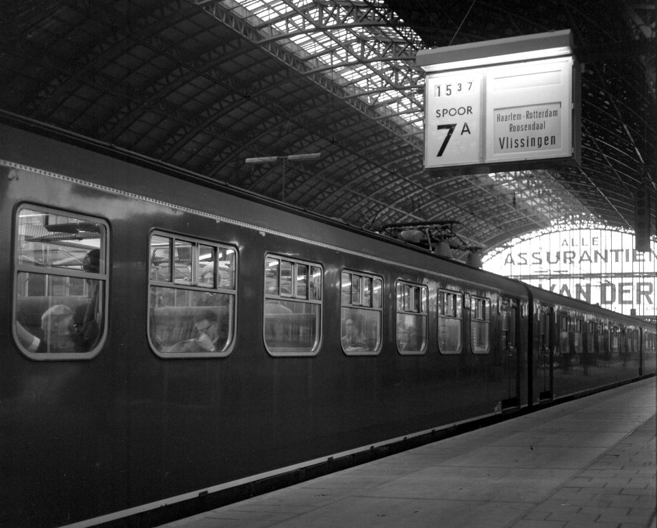 HUA-151091-Afbeelding van een electrisch treinstel plan P (mat. 1954) van de N.S. langs het perron van het N.S.-station Amsterdam C.S. te Amsterdam, met rechtsboven een centrale treinaanwijzer (CTA)