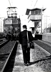 HUA-151112-Afbeelding van de electrische locomotief nr 1102 (serie 1100) van de N.S. opgesteld in de zak (een kopspoor) met op de voorgrond een machinist met tas en op de achtergrond seinhuis A van het N.S.-stat