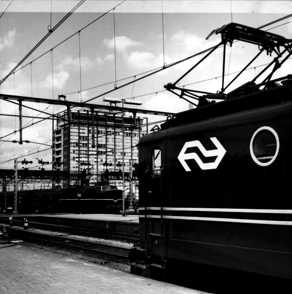 HUA-151717-Afbeelding van een electrische locomotief uit de serie 1100 langs een perron van het N.S.-station Amsterdam C.S. te Amsterdam. Op de achtergrond staat een electrische locomotief uit de serie 1200 met 