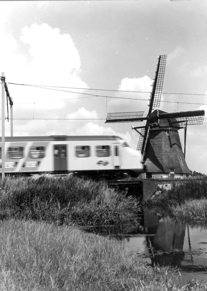 HUA-151021-Gezicht op een molen en een passerend electrisch treinstel mat. 1964 (plan V) van de N.S. ter hoogte van Hazerswoude