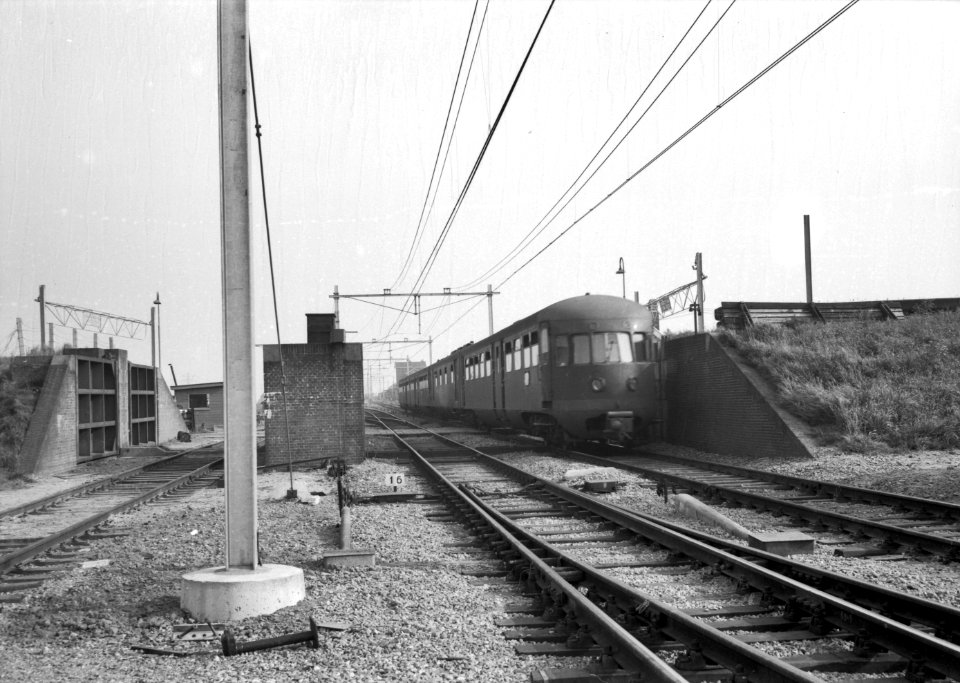 HUA-151190-Afbeelding van een diesel-electrisch treinstel DE 5 (serie 181-197, voorheen serie 51-68) van de N.S. door de dijkcoupure bij het N.S.-station Kruiningen-Yerseke