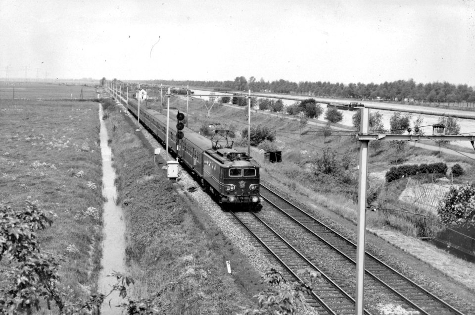HUA-150986-Afbeelding van de electrische locomotief nr 1142 serie 1100 met rijtuigen van de NS ter hoogte van Loenen aan de Vecht Op de achtergrond het Amsterdam