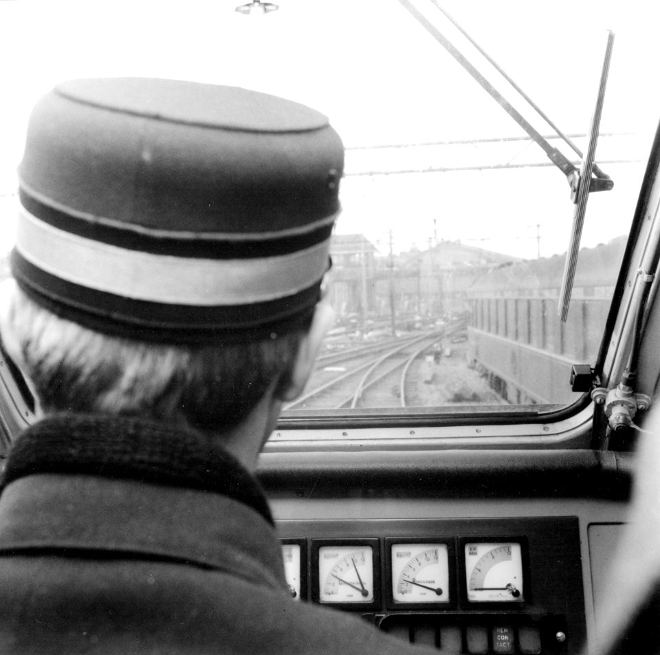HUA-171816-Gezicht over de schouder van de machinist in de cabine van een electrisch treinstel plan T mat 1964 van de NS op het emplacement bij Amsterdam CS